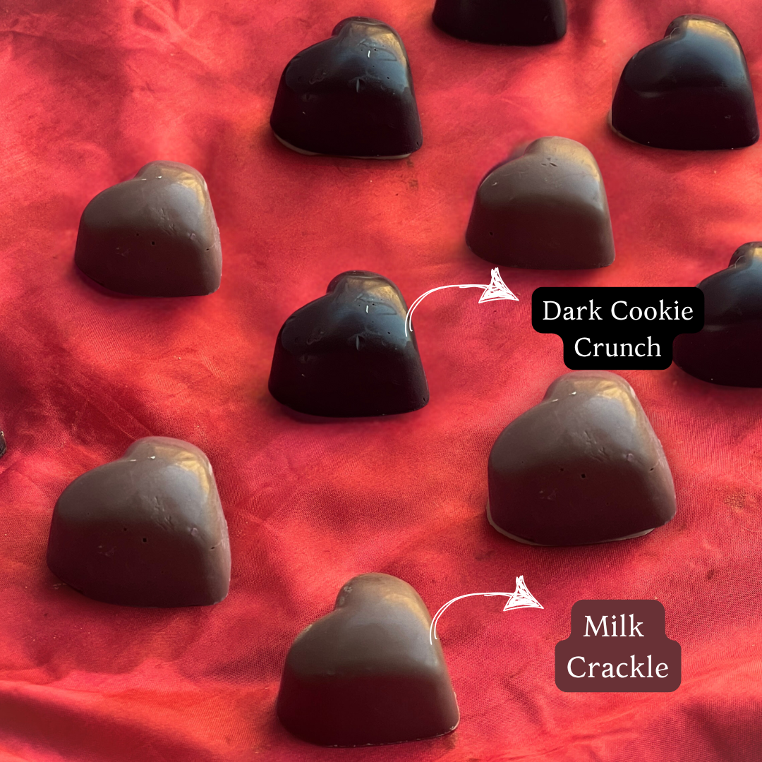 A side shot of our wedding chocolate hamper contents - dark cookie crunch dark chocolates and milk chocolate crackles placed on a red cloth and in a heart-shaped mould. 